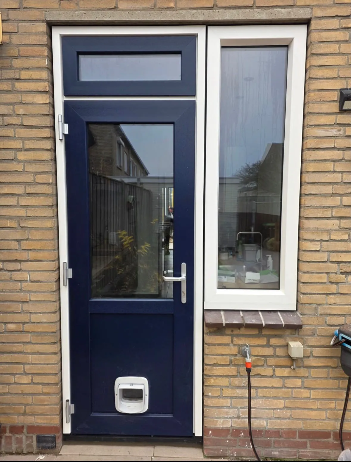 Donkerblauwe achterdeur met glas en een hoog zijraam