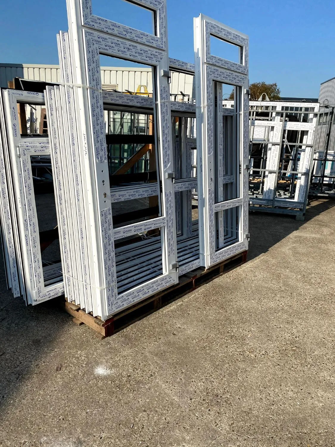 Witte kunststof kozijnen en deuren op pallets, klaar voor levering aan een project