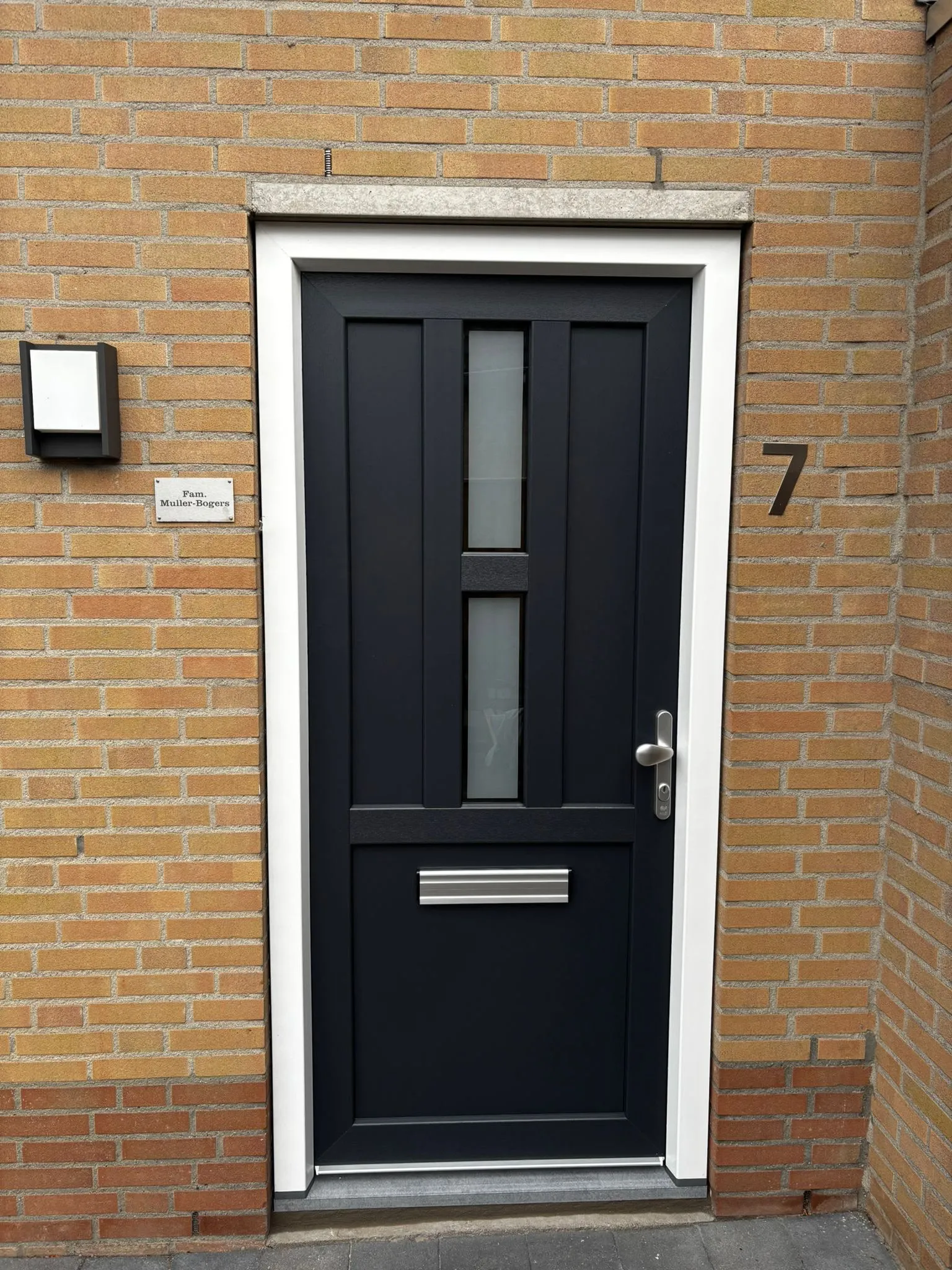 Antraciet voordeur met glasstroken in een bakstenen gevel
